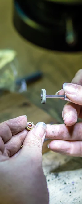 A craftsman polishing a small, circular jewellery piece with a rotary tool under focused lighting in a workshop setting. A craftsman polishing a small, circular jewellery piece with a rotary tool under focused lighting in a workshop setting.